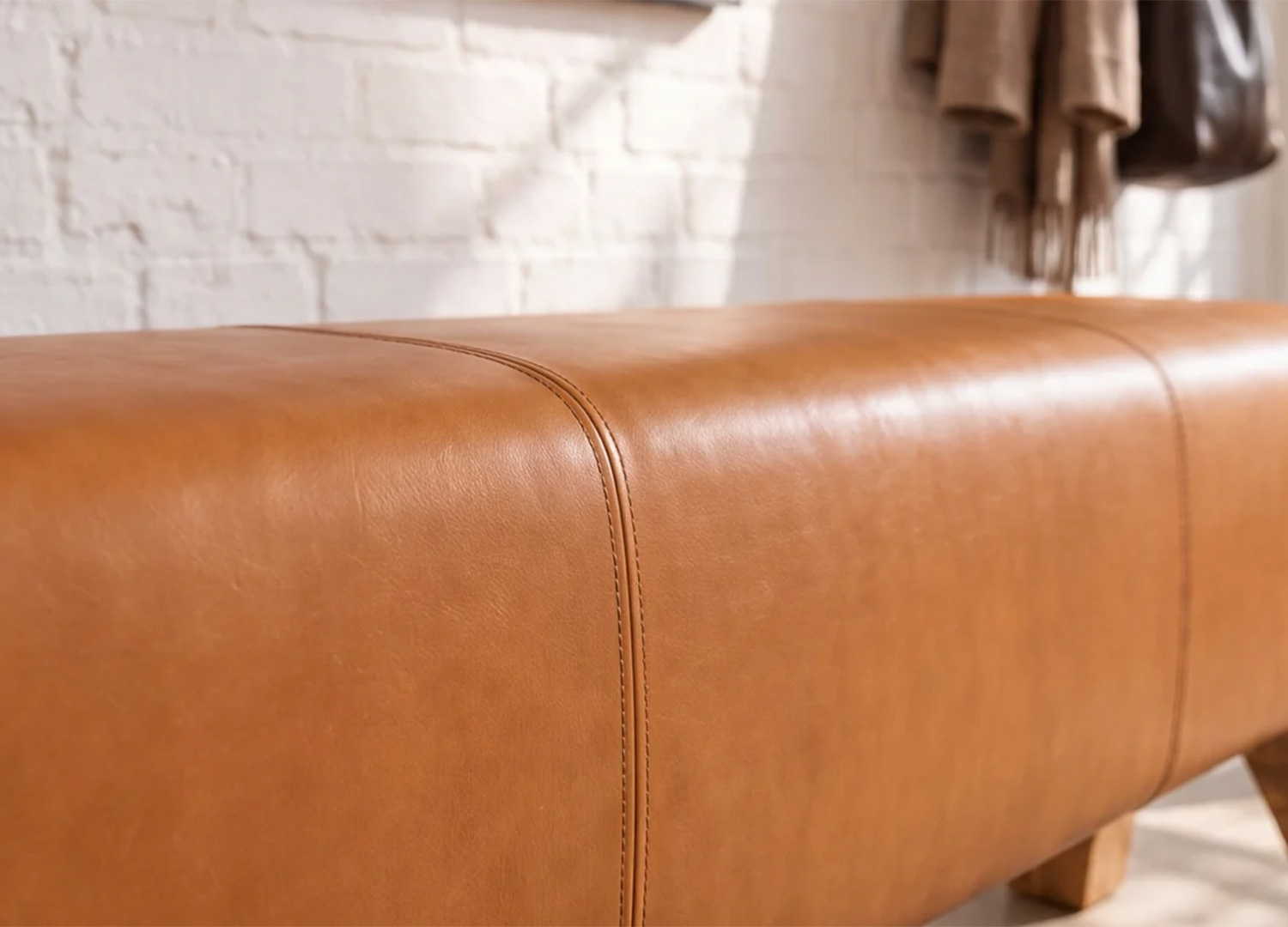 Gros plan sur les surpiqûres et la texture de l’assise en cuir cognac du banc CALVEO