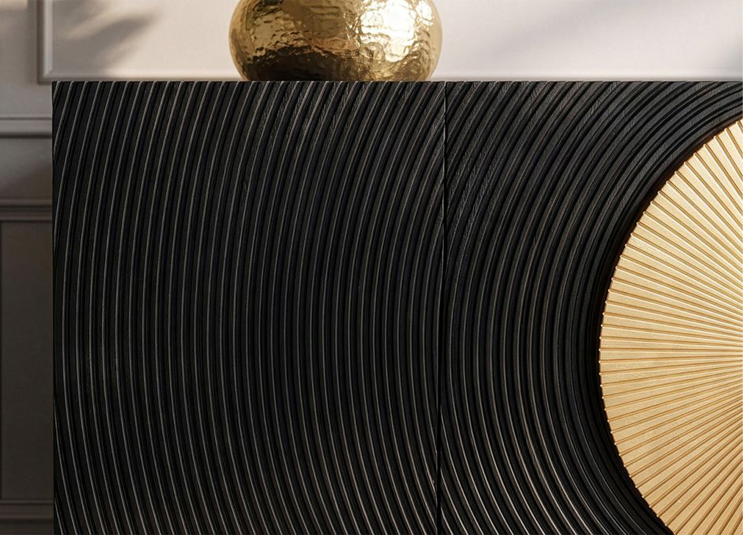 Gros plan sur la façade noire rainurée et le décor circulaire doré en relief du buffet