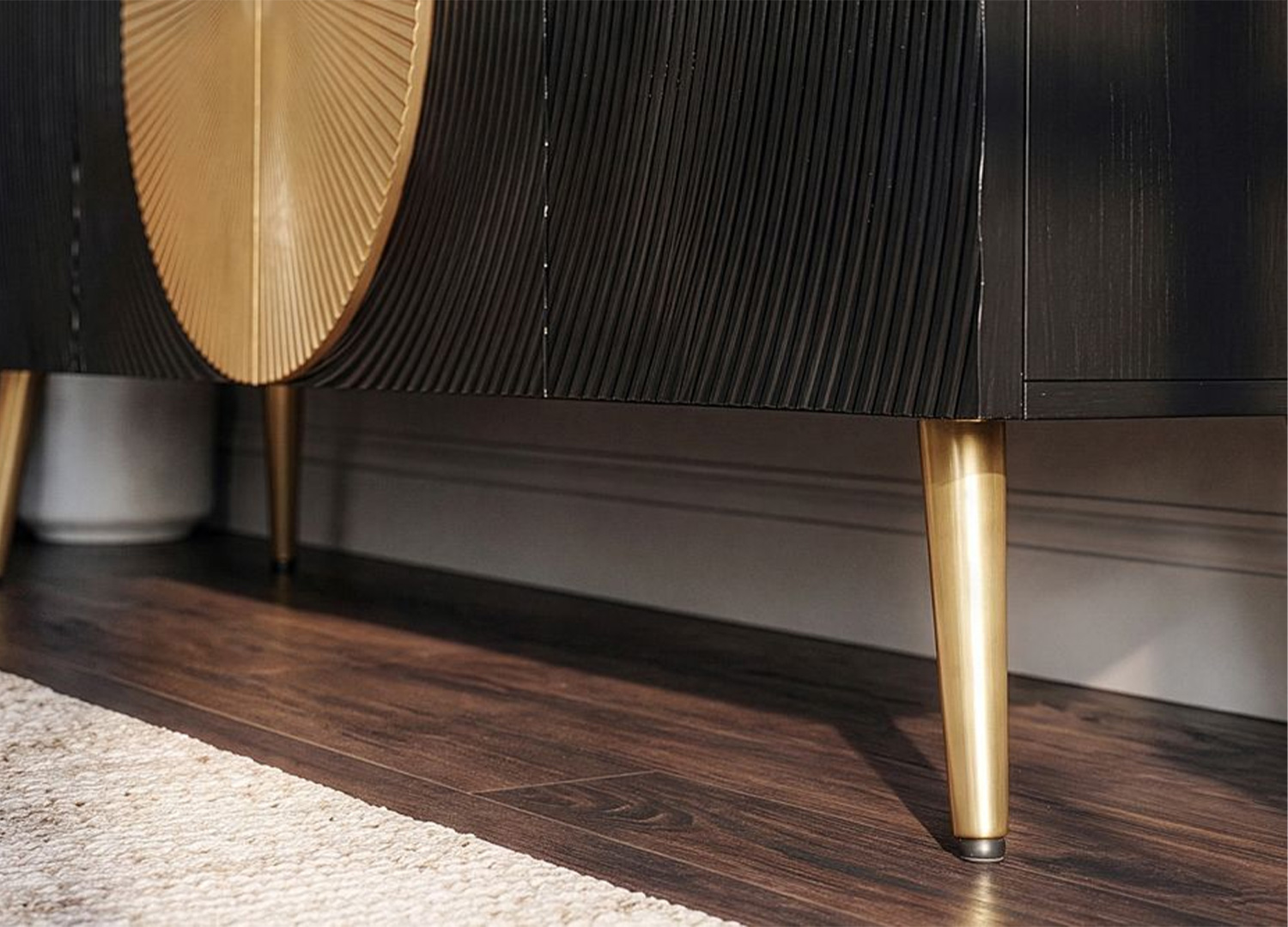 Gros plan sur les pieds métalliques dorés inclinés et le bas de la façade du buffet noir