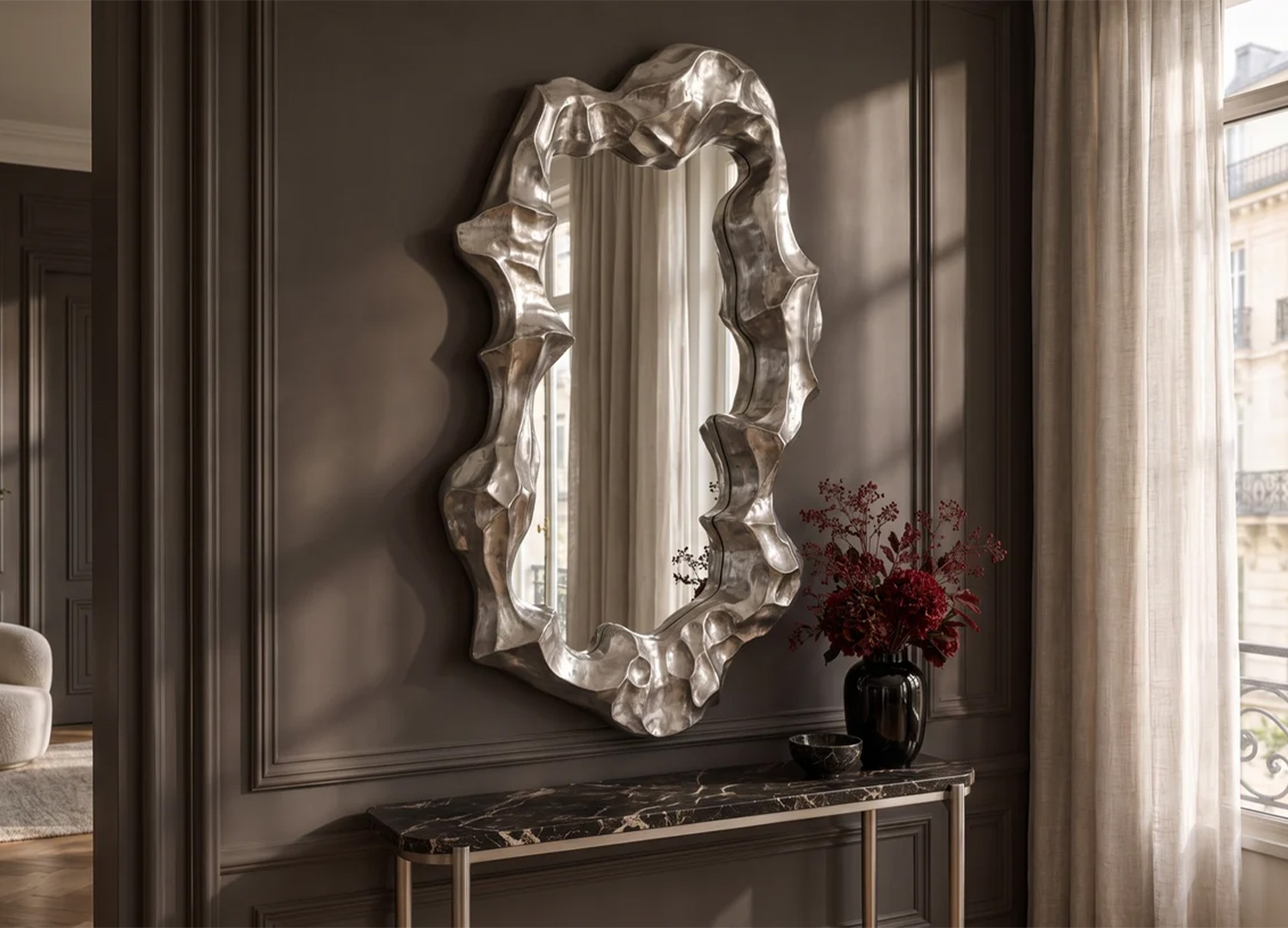 Grand miroir mural argenté aux contours organiques au-dessus d’une console en marbre noir