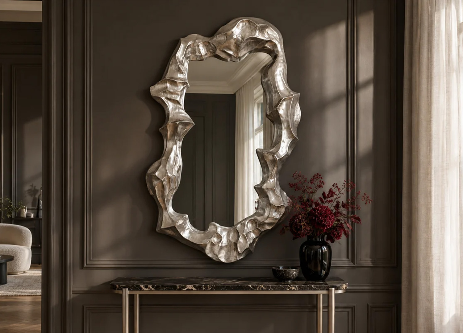 Miroir vertical argenté aux formes organiques accroché au-dessus d’une console dans une entrée élégante