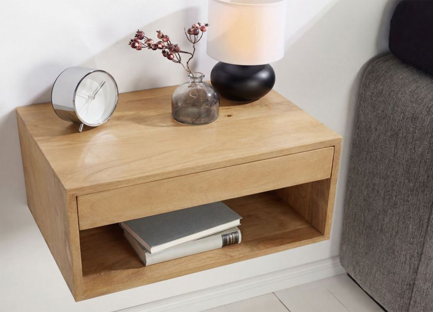Table de chevet murale en bois naturel décorée d’une lampe, d’un réveil et de livres